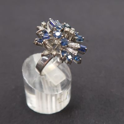a close up of a diamond and sapphire cluster ring on a clear acrylic base