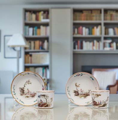 two cups and saucers sitting on a table in front of a bookshelf