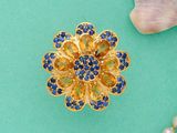 broche représentant une fleur dorée et bleue ornée de perles sur fond turquoise