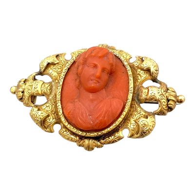 une image représentant une broche rouge et dorée sur laquelle figure le visage d'une femme