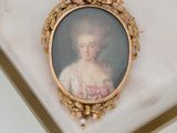 portrait d'une femme en robe blanche, dans un cadre doré, posé sur une surface en marbre