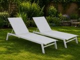 two white chaise loungers sitting in the grass in a garden