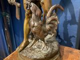 bronze statue of a man with a rooster on a wooden table