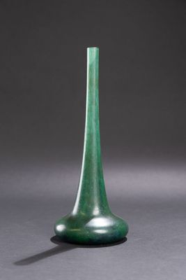 green glass vase on a gray surface with a shadow on the ground