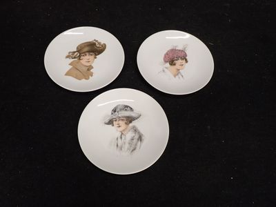 trois assiettes sur lesquelles figurent des images de femmes coiffées de chapeaux, posées sur un fond noir