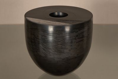 un vase noir posé sur une table, avec un mur blanc en arrière-plan