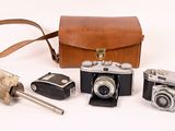 several old cameras and a leather case on a white surface