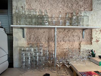 bottles and glasses on a shelf in front of a wall