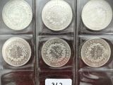 six pièces d'argent dans une vitrine, accompagnées d'une étiquette de prix