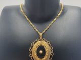 a gold necklace with a black stone on a mannequin