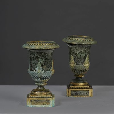 pair of antique bronze urns on pedestals against a gray background