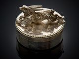 an antique silver box with a dog on it on a black surface