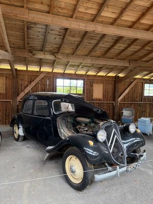 Plusieurs vieilles voitures sont garées dans un garage au plafond en bois.