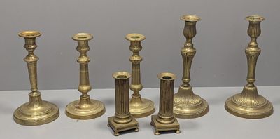 six brass candlesticks are lined up on a white surface