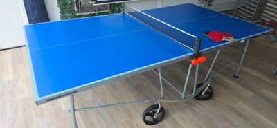 une table de ping-pong bleue sur laquelle sont posées deux raquettes rouges
