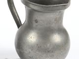 un pichet en argent posé sur une surface blanche, à côté d'une tasse