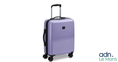La valise violette repose sur ses roulettes, posée sur une surface blanche.