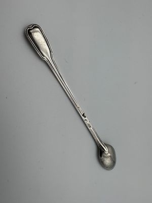 une cuillère en argent posée sur une surface blanche, d'où dépasse une petite cuillère