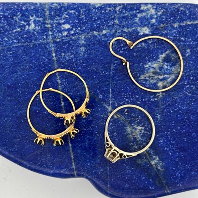 three pairs of gold hoop earrings sitting on a blue stone