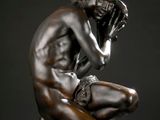 une statue en bronze représentant une femme assise sur un socle, la main posée sur le visage