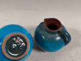 a person holding a small blue vase next to a smaller blue vase