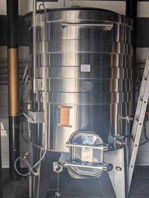 une grande cuve en acier inoxydable, avec une échelle à côté