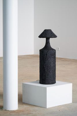 une image représentant une sculpture noire posée sur un socle blanc dans une pièce