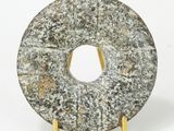 un beignet en pierre posé sur un socle doré, sur fond blanc