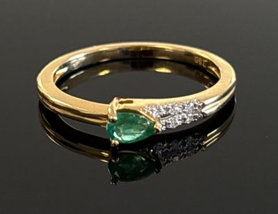 an emerald and diamond ring on a black surface with reflection