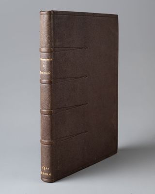 un livre en cuir marron avec des bordures dorées sur fond gris