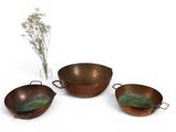 three copper pans and a vase with flowers on a white surface