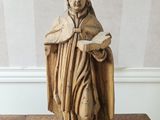 statue en bois représentant un homme tenant un livre posé sur une table en bois