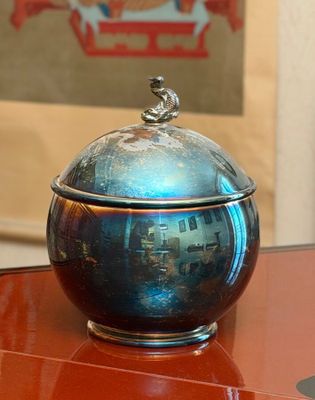 a silver bowl sitting on a table with a picture in the background