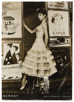 photographie en noir et blanc d'une femme en robe, debout devant des affiches