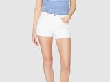 a woman in a striped shirt and white shorts stands in front of a gray background
