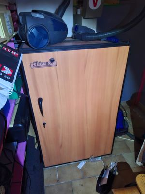 une petite armoire sur laquelle est posé un aspirateur, dans une pièce encombrée