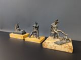 trois sculptures en bronze représentant un homme et une femme assis sur une chaise