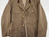 La veste est de couleur beige clair et comporte des boutons dorés au niveau du col.