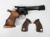 un vieux revolver et deux crosses en bois posés sur une surface blanche