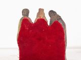figurines of three people sitting on a red pillow on a white surface