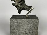 une sculpture en bronze représentant un chien posé sur un socle, sur fond blanc