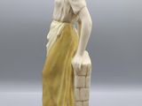 an antique figurine of a woman sitting on a ledge