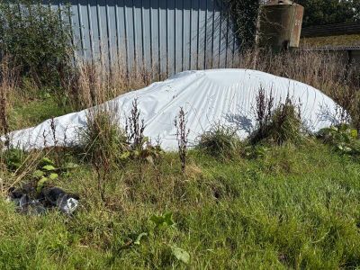 a white tarp covering a car in the grass