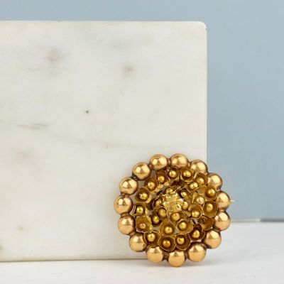 un gros plan d'une broche en forme de fleur en or posée sur un bloc de marbre