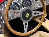 dashboard of a red sports car with a wooden steering wheel and gauges