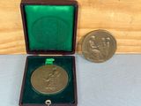 une médaille d'or dans un coffret en bois, à côté d'une petite pièce de monnaie