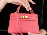 woman ' s hand holding a pink leather handbag with gold hardware