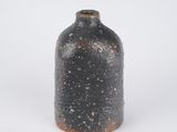 a black vase with a brown top sitting on a white surface