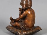 bronze figurine of a boy sitting on a pillow holding a cell phone