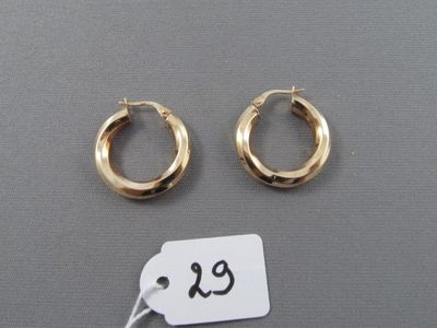 deux paires de boucles d'oreilles créoles en or, avec une étiquette de prix posée sur une surface grise